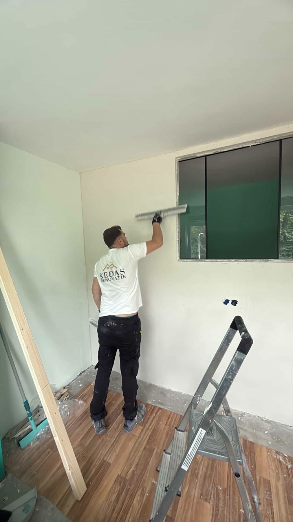 Kedas Renovatie vakman in bedrijfsshirt werkt strak stucwerk af op de bouwplaats