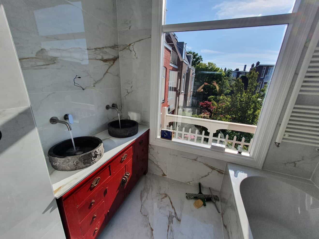 Calacatta badkamer met rode vintage kast en grachtraam uitzicht in Rotterdam