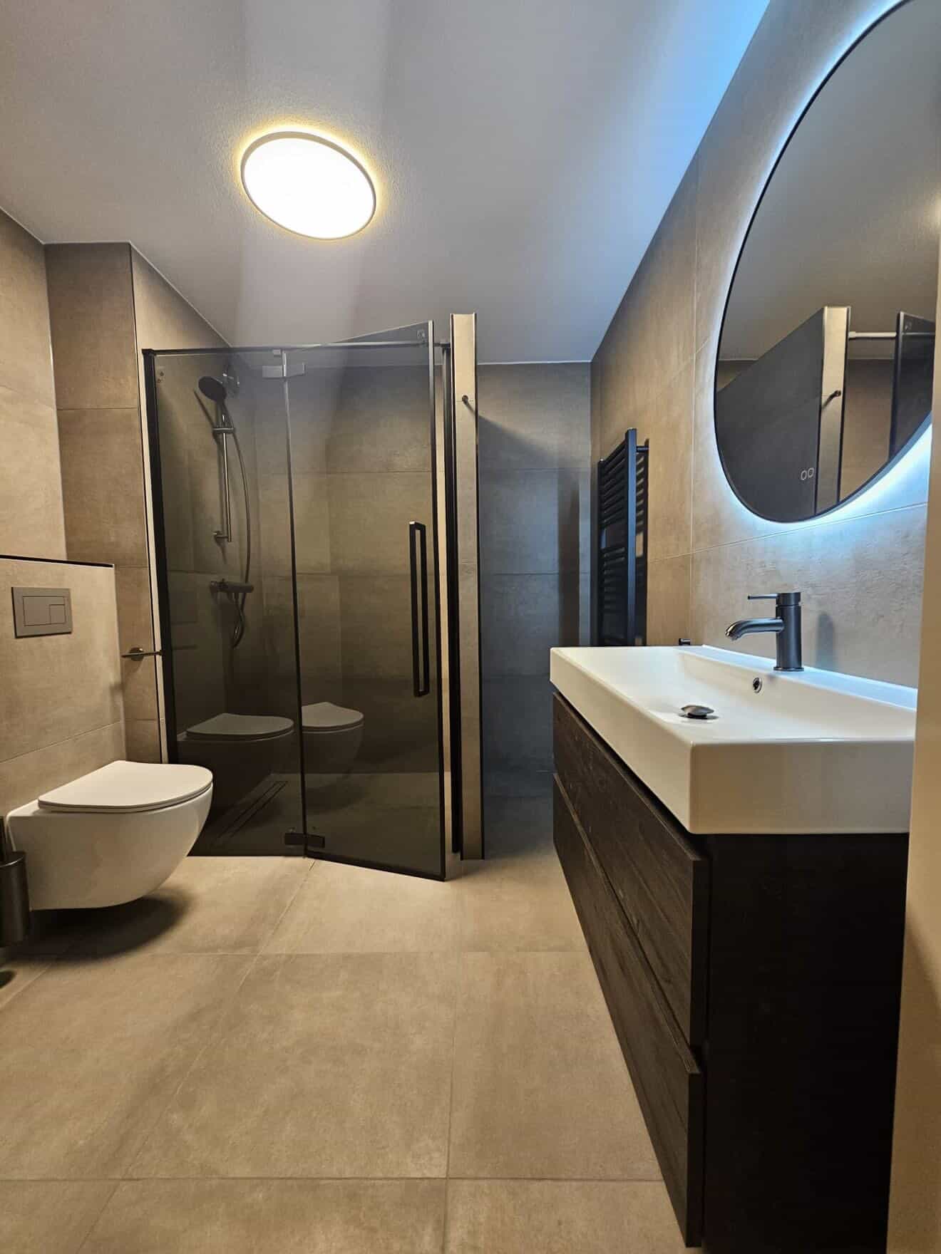 Beton-look badkamer met donkere houten vanity en ronde backlit spiegel